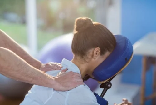 image-asset-min-768×517 A woman lying facedown on a massage chair with her head supported that is being treated by a chiropractor on her neck.