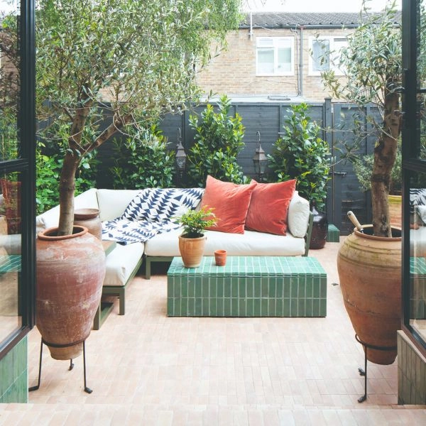 Μικρός κήπος με γωνιακό καναπέ εξωτερικού χώρου και μεγάλες πήλινες γλάστρες