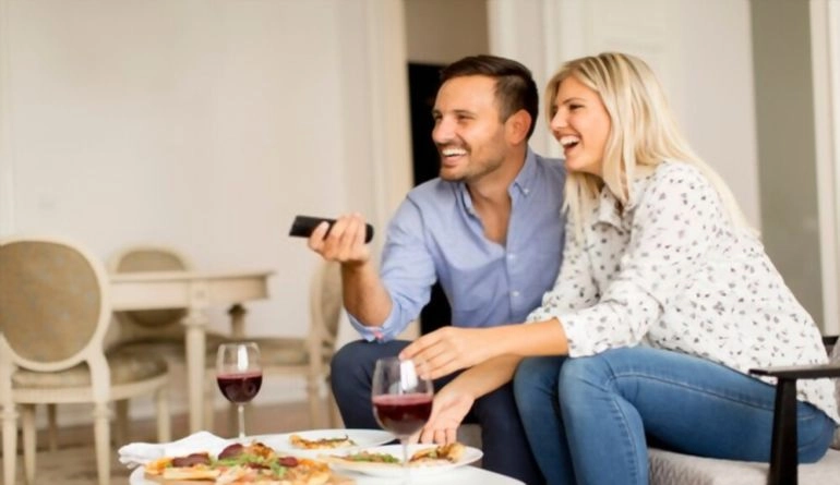 Επέτειος γάμου: 9 ιδέες για να γιορτάσετε την αγάπη σας 3 Νεαρό ζευγάρι τρώει πίτσα και βλέπει τηλεόραση στο σπίτι