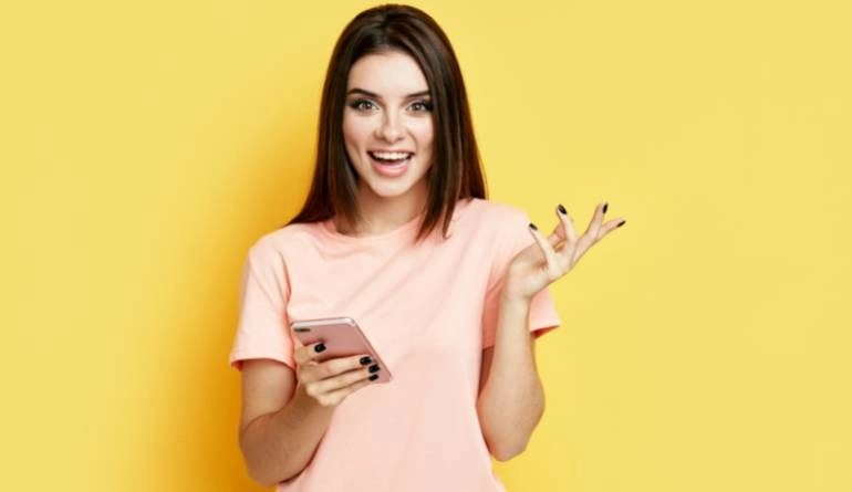 Πως να εγγραφώ/συνδεθώ στο WedMyWay 1 Χαρούμενη κοπέλα κρατάει κινητό τηλέφωνο σε κίτρινο φόντο