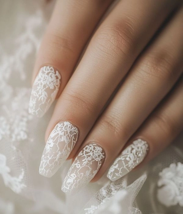 Νυφικά νύχια με λευκά σχέδια δαντέλας που ταιριάζουν με το νυφικό φόρεμα, σε μακρύ σχήμα.