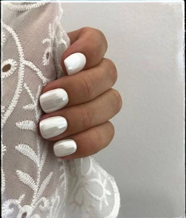 Λευκά νυφικά νύχια με περλέ φινίρισμα, σε οβάλ σχήμα, που ταιριάζουν με ένα λευκό δαντελένιο φόρεμα.