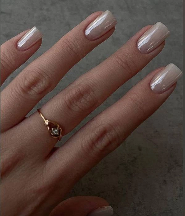 Νυφικά νύχια σε nude περλέ χρώμα, σε τετράγωνο σχήμα, με ένα χρυσό δαχτυλίδι με διαμάντι.