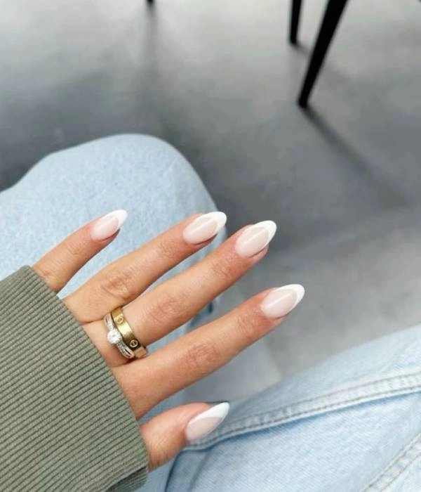 Νύχια με γαλλικό μανικιούρ και δύο δαχτυλίδια Cartier Love, φορεμένα σε χαλαρή εμφάνιση με τζιν και πράσινο πουλόβερ.