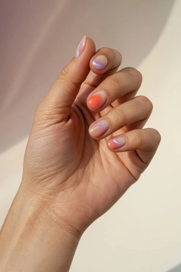 Γυναικεία χέρια με ημιμόνιμο μανικιούρ σε παστέλ αποχρώσεις πορτοκαλί, ροζ και λιλά με απαλές ombre γραμμές