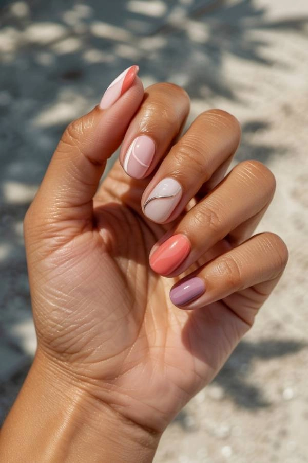 Γυναικεία χέρια με ημιμόνιμο μανικιούρ σε παστέλ ροζ, κοραλλί και λιλά αποχρώσεις, με μοντέρνα μεταλλικά σχέδια σε χρυσό και ασημί