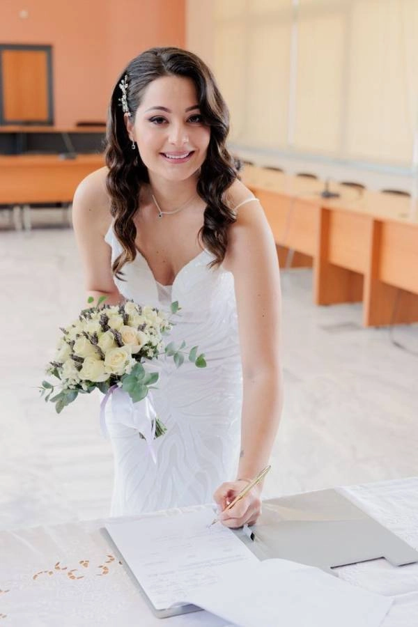 Η νύφη υπογράφει τα έγγραφα του πολιτικού γάμου, χαμογελώντας στην κάμερα.