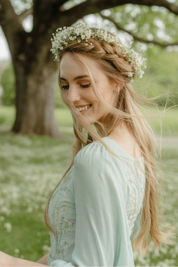 11 Χτενίσματα για κουμπάρα που θα κλέψουν την παράσταση 9 Κουμπάρα με crown braid και ανάλαφρο φόρεμα, σε ανοιξιάτικο εξωτερικό γάμο.