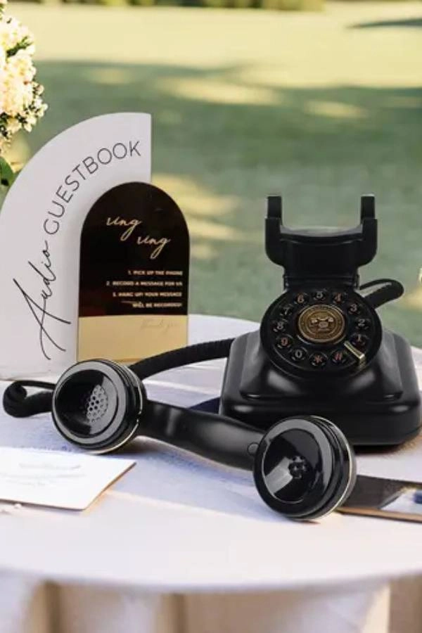 Γάμος 2025: 10+ τάσεις που θα λατρέψουν οι μέλλουσες νύφες 13 Διακόσμηση γάμου με μαύρο ρετρό τηλέφωνο σε τραπέζι ως audio guest book, πλαισιωμένο από λουλούδια και πίνακα οδηγιών