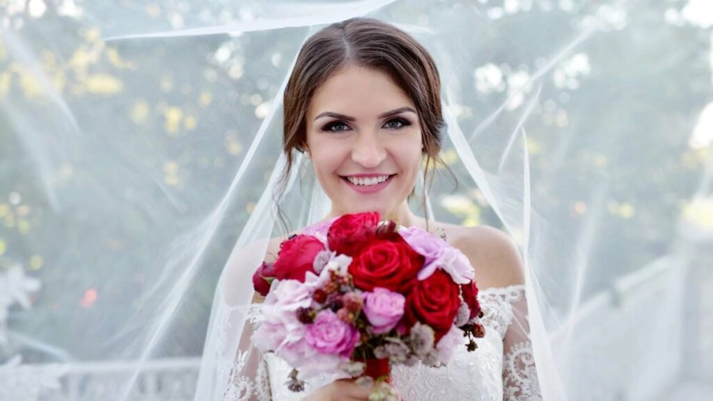 Χαμογελαστή νύφη με πέπλο και κόκκινο-ροζ μπουκέτο, bridal εμφάνιση για νυφικό χτένισμα 2025 – φωτογραφία από την Κατερίνα Γιαννουζάκου