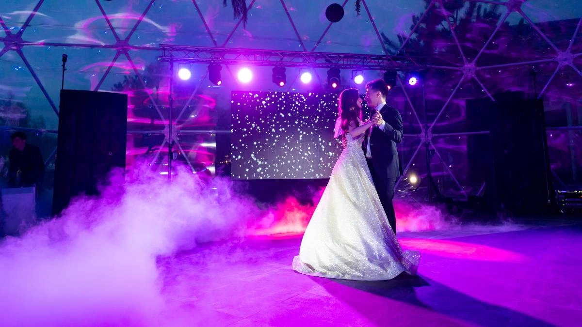 Το ζευγάρι χορεύει τον πρώτο του χορό σε δεξίωση γάμου με ρομαντικό φωτισμό και μουσική υπόκρουση, δημιουργώντας μαγική ατμόσφαιρα.