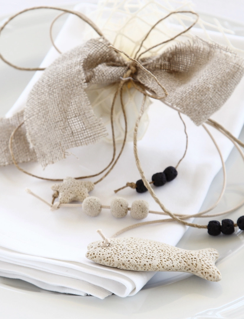 Μπομπονιέρα γάμου σε λευκή πετσέτα με φυσικά υλικά, λινό φιόγκο και χειροποίητα διακοσμητικά σε μορφή ψαριού, από τη Vassiliki Creations