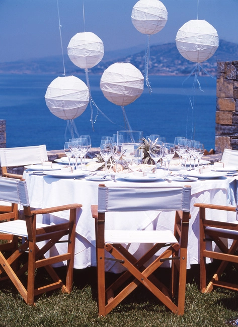 Καλοκαιρινή διακόσμηση γάμου σε εξωτερικό χώρο με θέα τη θάλασσα, λευκά φαναράκια, ναυτικό ύφος και minimal στρώσιμο τραπεζιού, από τη Vassiliki Creations