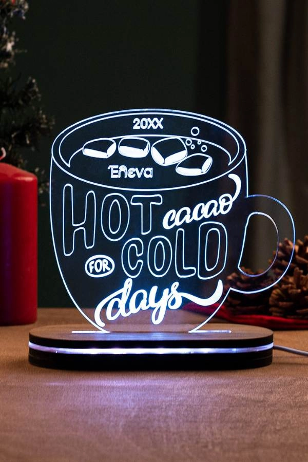 LED φωτιστικό ακρυλικό σε σχήμα κούπας με το μήνυμα “Hot cacao for cold days”, ξύλινη βάση και απαλή λευκή λάμψη σε ζεστό εσωτερικό σκηνικό.
        loading=