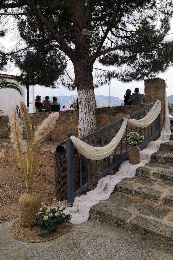 Boho στολισμός εκκλησίας σε εξωτερικό χώρο με pampas grass, ψάθινα στοιχεία, λινό ύφασμα και φυσική παλέτα, δημιουργώντας χαλαρή και ρομαντική ατμόσφαιρα.