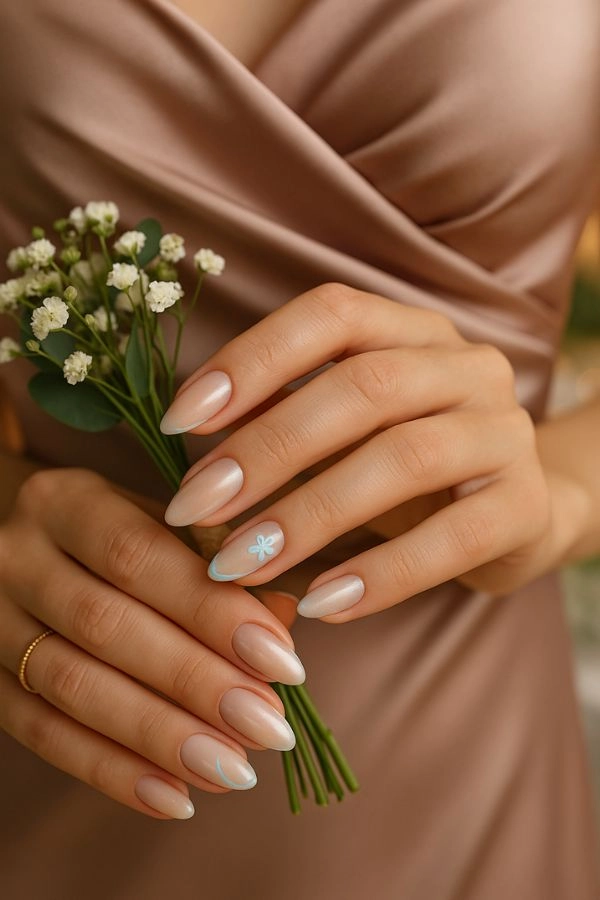 Νύχια για γάμο: Ιδέες για καλεσμένη κουμπάρα και πεθερά 4 Νύχια για γάμο κουμπάρα σε μεσαίο almond μήκος με nude βάση και διακριτικό chrome, λεπτή baby blue γραμμή και μικρό λουλουδάκι, κοντινό πλάνο με σατινέ φόρεμα και ανθοδέσμη.