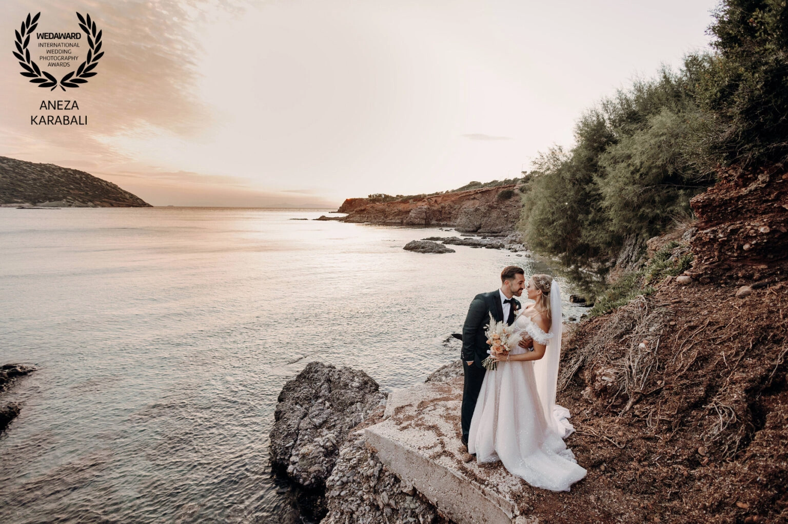 Ζευγάρι αγκαλιασμένο σε βραχώδη ακτή κατά τη δύση του ήλιου