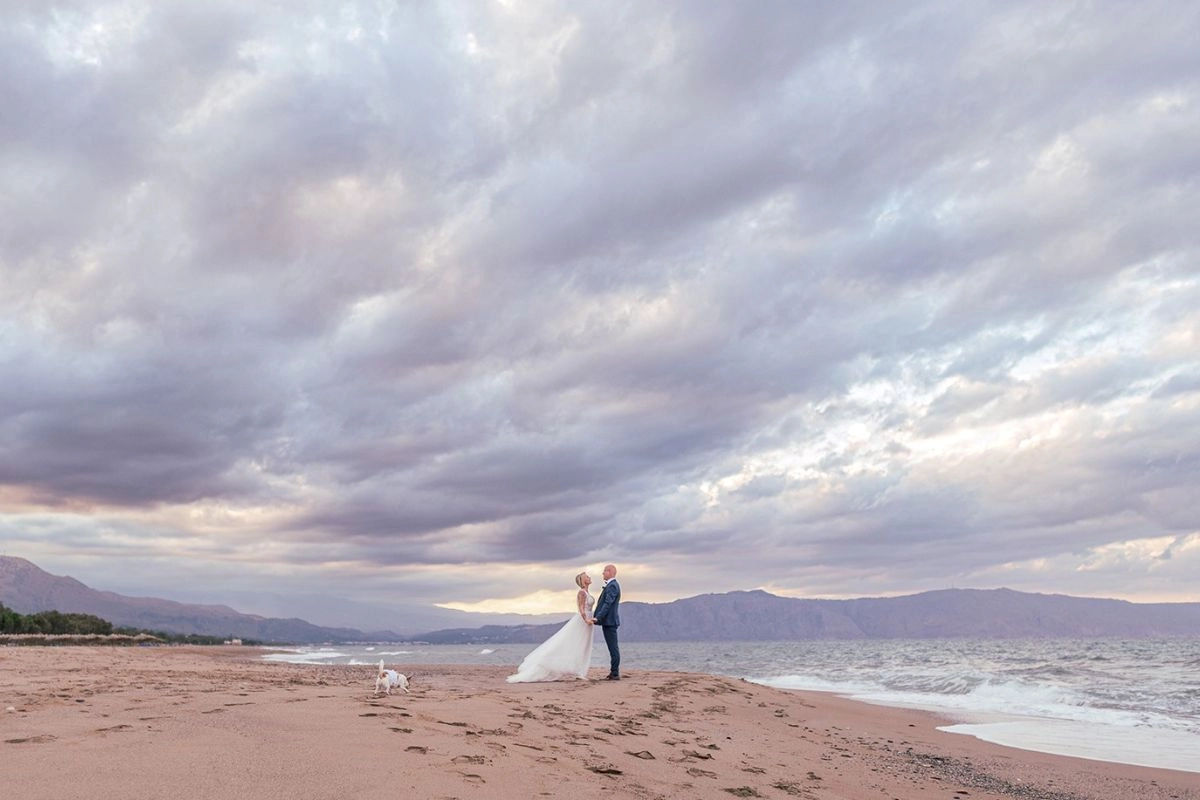 Νεόνυμφο ζευγάρι στην παραλία με φόντο τη θάλασσα και τον συννεφιασμένο ουρανό
