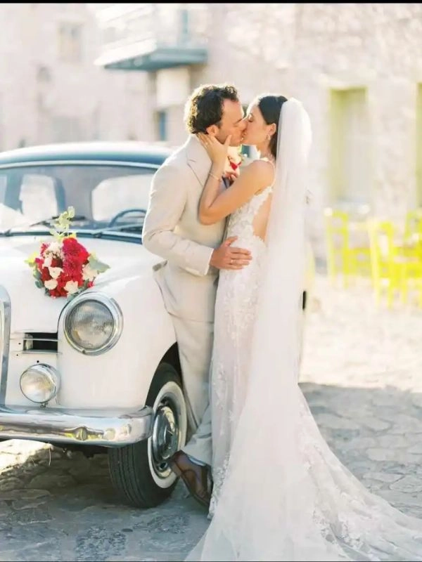 Νεόνυμφο ζευγάρι μπροστά από κλασικό αυτοκίνητο γάμου σε παραδοσιακό χωριό